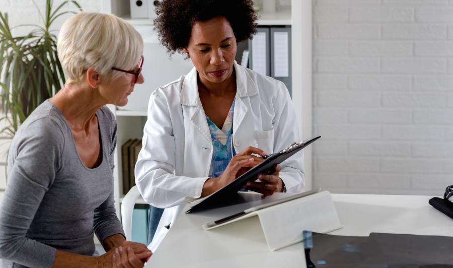 Female doctor with clipboard and female patient sitting together in medical office