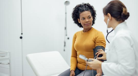 Doctor measuring blood pressure to a smiling woman as part of a medical exam.